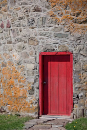 A bright red wooden door frames the entrance to a stone building